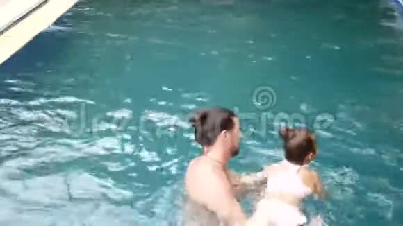 幸福的家庭活泼的父亲带着小孩子可爱的蹒跚学步的女儿在游泳池里玩得很开心视频的预览图