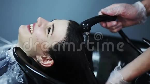 理发师戴着手套在美容店里洗着黑发女孩的头发视频的预览图