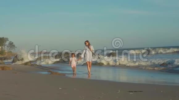 母亲带着婴儿在海边慢动作地牵着手走着视频的预览图