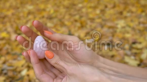 女性手用橙色指甲手拿粉红色石英黄色的鸡蛋以供Vumfit模仿或冥想黄色的跌倒视频的预览图