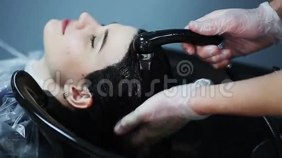 理发师戴着手套在美容店里洗着黑发女孩的头发视频的预览图