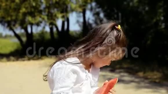 快乐开朗的小女孩穿着白色连衣裙在海滩上玩得开心吃西瓜视频的预览图