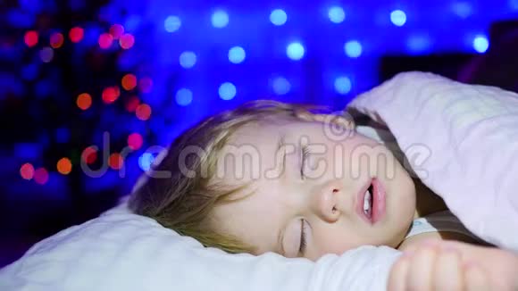 美丽的婴儿睡在床上圣诞夜背景中冷杉的灯光和花环视频的预览图