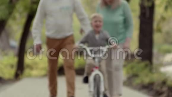 真正的幸福家庭在公园里休息一个小男孩骑着自行车早秋在公园的生活方式家庭视频的预览图