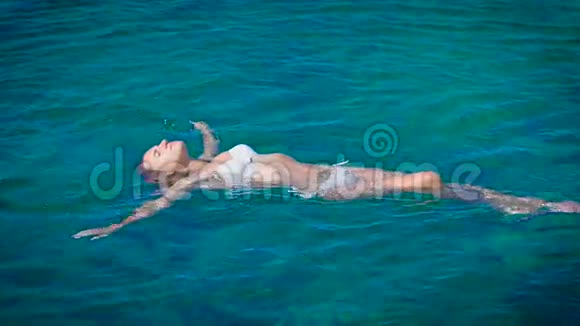 穿着白色比基尼在蔚蓝的大海中游泳的年轻快乐女人视频的预览图
