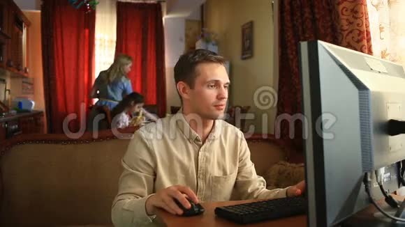 丈夫坐在社交网络中的电脑前而妻子和孩子则在厨房里忙碌丈夫有视频的预览图