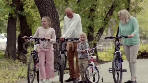 真正的幸福家庭在公园里休息一个小男孩骑着自行车早秋在公园的生活方式家庭视频的预览图