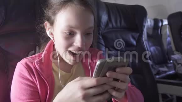 快乐的少女在飞机机舱里玩智能手机游戏还在旅行股票录像视频的预览图