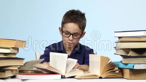 戴眼镜的男孩坐在一张桌子旁兴奋地在寻找蓝色背景视频的预览图