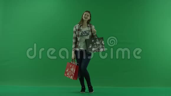 女孩站在绿色的屏幕上拿着购物袋微笑视频的预览图