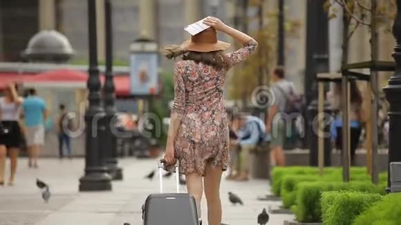 快乐的年轻女游客拿着票和手提箱走在城市的街道上视频的预览图