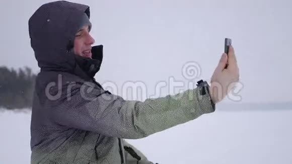 男人自拍选择一个方便的角度在白雪覆盖的湖泊和森林的背景下4K视频的预览图