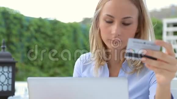 有着笔记本电脑和信用卡的年轻女人坐在咖啡馆里视频的预览图