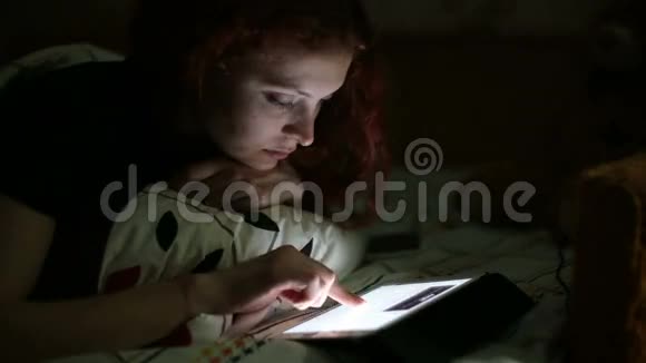 带着平板电脑的年轻女子晚上躺在家里的床上时收到了一条短信视频的预览图