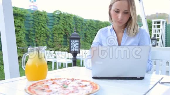 年轻女性使用笔记本电脑坐在城市咖啡馆里吃披萨视频的预览图