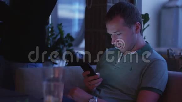 穿绿色衬衫的男人坐在沙发上在夜总会聚会上用电话作弊视频的预览图