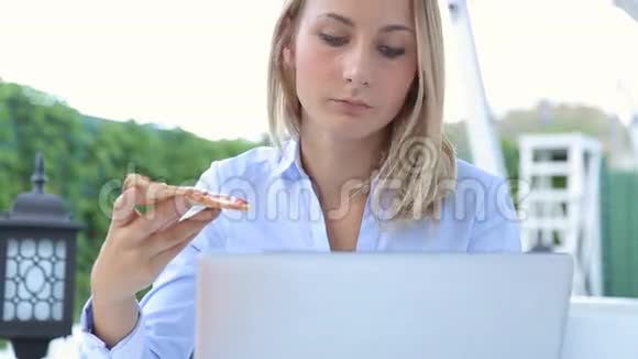 年轻女性使用笔记本电脑坐在城市咖啡馆里吃披萨视频的预览图