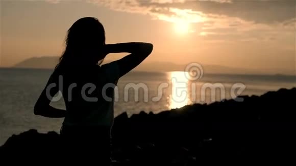 美丽的年轻女性在夕阳下仰望大海和举起双手的剪影视频的预览图