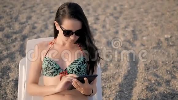 年轻美丽的女子游泳衣使用平板电脑在大理石海滩视频的预览图