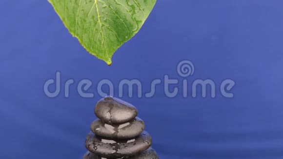 从一片绿叶上滴下的水滴落在一个由黑色石头做成的金字塔上视频的预览图