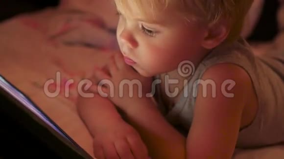 男孩躺在毯子下在触摸板上看卡通特写视频的预览图