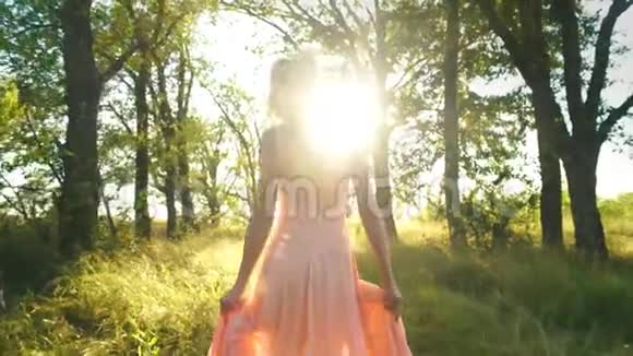 美丽的金发女郎穿着桃色的裙子在树林里散步玩得很开心视频的预览图
