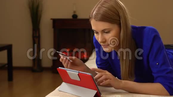 美丽迷人的年轻女子躺在沙发上用信用卡在网上买东西视频的预览图