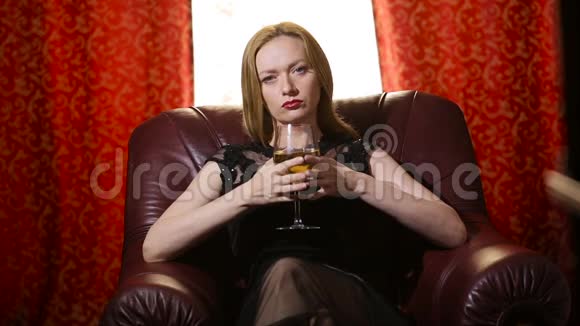 一个穿着黑色连衣裙嘴唇上涂着红色口红的致命女人坐在一张皮椅上手里拿着一杯白葡萄酒视频的预览图