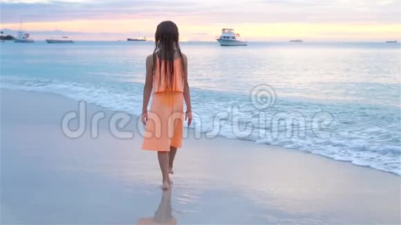 可爱的快乐小女孩在日落时走在白色的海滩上流动人口视频的预览图