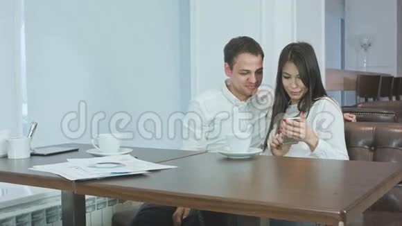 两个办公室同事在咖啡馆里看着手机上的照片笑了视频的预览图
