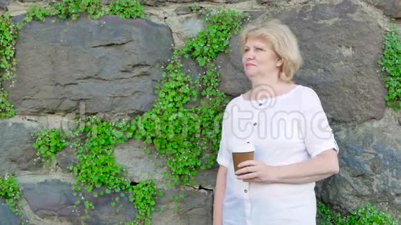 喝咖啡的老年妇女背景中野生石头的复古墙视频的预览图