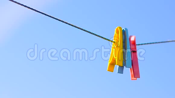 彩色衣服钉在亚麻绳上摆动在蓝天的背景上视频的预览图