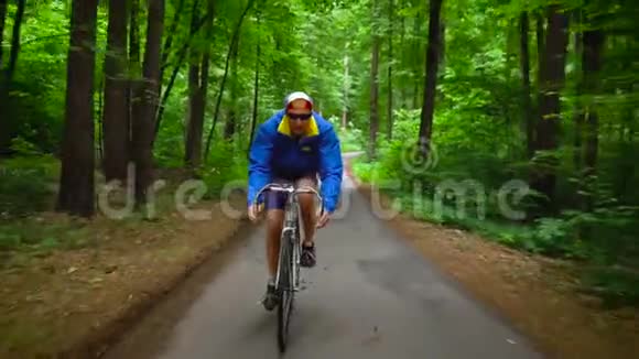 中年男子正沿着一条森林道路骑自行车动作缓慢视频的预览图