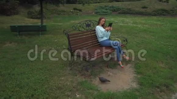 一个长发少女坐在公园的长椅上拿着平板电脑微笑着视频的预览图