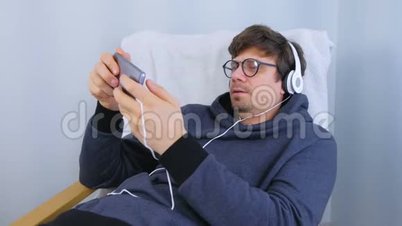 戴着眼镜和耳机的人在智能手机里玩游戏玩家放松视频的预览图