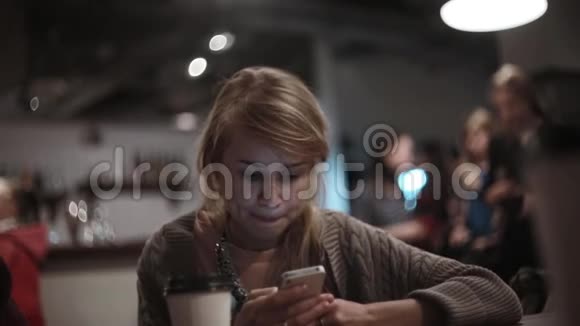 年轻漂亮的女人坐在咖啡馆里用智能手机有魅力的女性浏览互联网视频的预览图