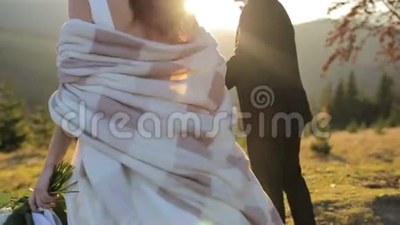 年轻漂亮的新婚夫妇在日落时一起在山坡上可爱的新郎和新娘风视频的预览图