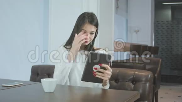 漂亮的年轻女子坐在咖啡馆里用平板电脑打视频电话视频的预览图