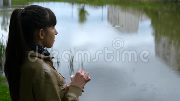 美丽的少女站在河堤上喝着一次性杯子里的外卖咖啡视频的预览图