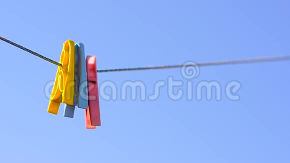 彩色衣服钉在亚麻绳上摆动在蓝天的背景上视频的预览图