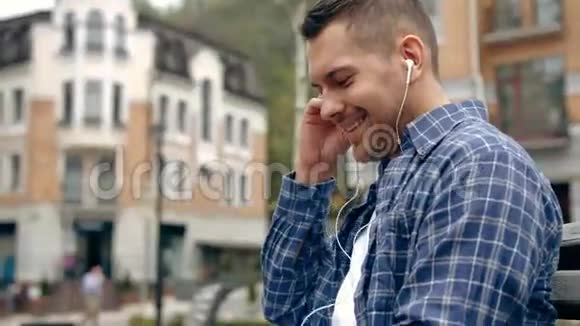 快乐的男人听着智能手机带来的音乐带着温暖的夕阳城市背景视频的预览图