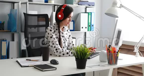 女商人戴着红色耳机在现代办公室里使用笔记本电脑视频的预览图