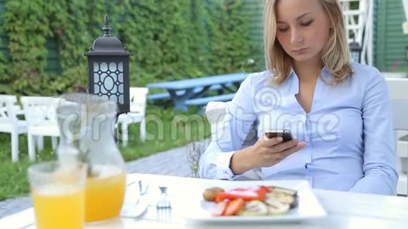 有魅力的年轻女子在户外餐桌上使用她的智能手机视频的预览图
