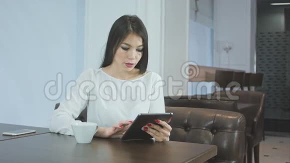 在咖啡馆喝咖啡或茶时使用数码平板电脑的年轻女性视频的预览图
