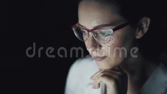 一个商务女性在笔记本电脑上工作到很晚的肖像带眼镜的屏幕反射视频的预览图