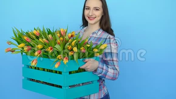年轻女子拿着一个蓝色背景上有郁金香的盒子视频的预览图