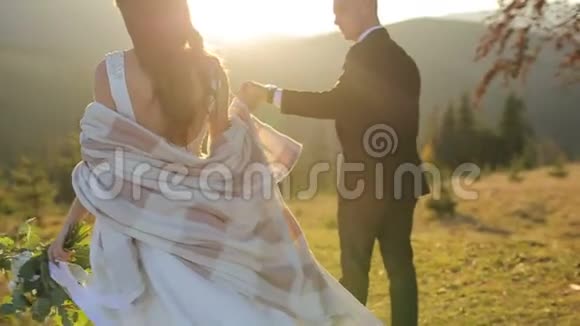 年轻漂亮的新婚夫妇在日落时一起在山坡上可爱的新郎和新娘风视频的预览图