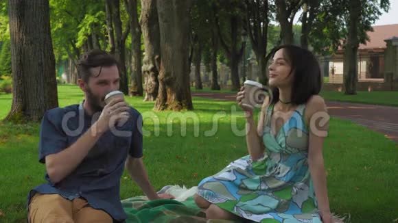 一个男孩和女孩在公园里举行了一次会议和野餐他们坐在草坪上说话喝咖啡微笑视频的预览图