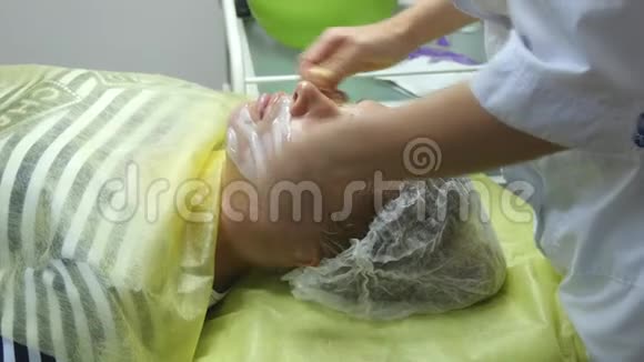 美容师在美容院把面膜敷在漂亮的女孩脸上有面部护理的女人使用口罩视频的预览图