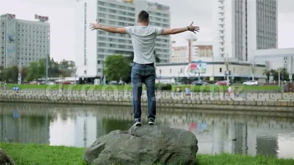 漂亮的年轻人站在河边的一块大石头上视频的预览图